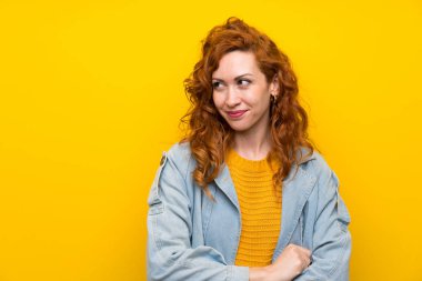 Izole sarı arka plan ayakta üzerinde Redhead kadın ve yan bakıyor