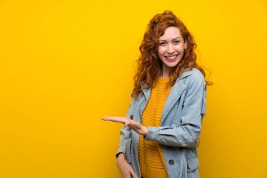 Redhead kadın izole sarı arka plan üzerinde gelmeye davet için yan ellerini uzatarak