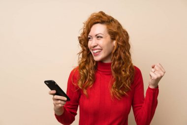 Cep telefonu kullanarak boğazlı kazak ile Redhead kadın