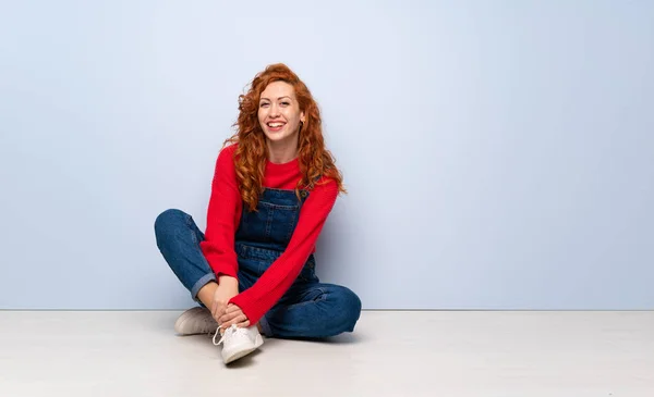 Redhead woman with overalls sitting on the floor laughing