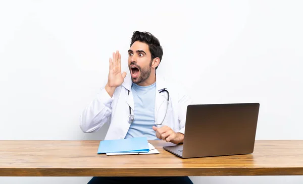 年轻的医生男子与他的笔记本电脑在孤立的墙上大喊大叫 张开嘴 — 图库照片