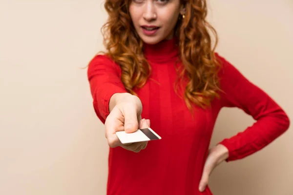 Redhead woman with turtleneck sweater holding a credit card