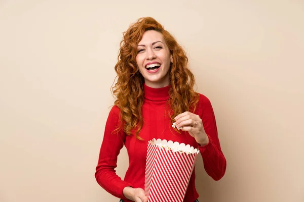 Redhead woman with turtleneck sweater holding a bowl of popcorns