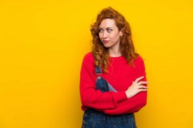 Izole sarı duvar ayakta ve bir fikir düşünme üzerinde tulum ile Redhead kadın