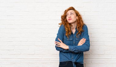 Omuzları kaldırırken şüpheler jest yapma beyaz tuğla duvar üzerinde Redhead kadın
