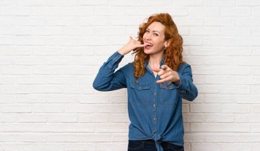 Beyaz tuğla duvar üzerinde Redhead kadın telefon jest yapma ve ön işaret