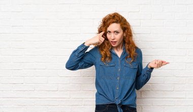 Beyaz tuğla duvar üzerinde Redhead kadın kafasına parmak koyarak delilik jest yapma