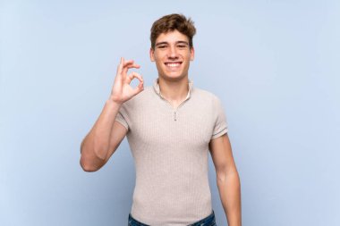 Izole mavi duvar üzerinde yakışıklı genç adam parmakları ile ok işareti gösteren