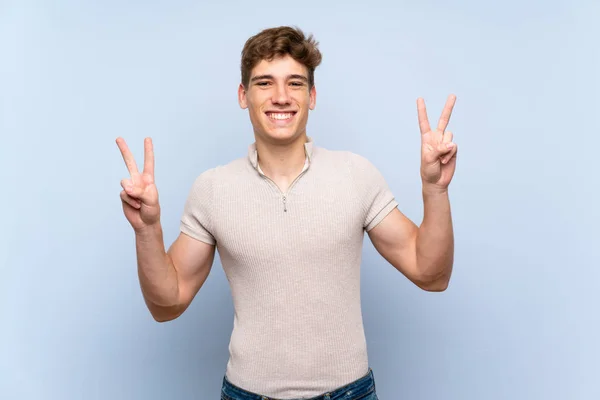 Beau Jeune Homme Sur Mur Bleu Isolé Montrant Signe Victoire — Photo