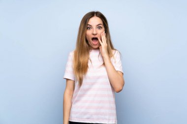 Soyutlanmış mavi arka planda, şaşırmış ve şok olmuş yüz ifadesi olan genç bir kadın.