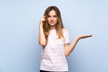 Izole mavi arka plan üzerinde genç kadın kafasına parmak koyarak delilik jest yapma