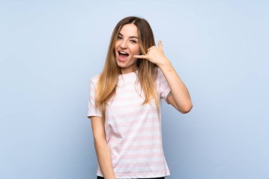 İzole edilmiş mavi arka planı olan genç bir kadın telefon jesti yapıyor. Bana geri dönüş işareti ver.