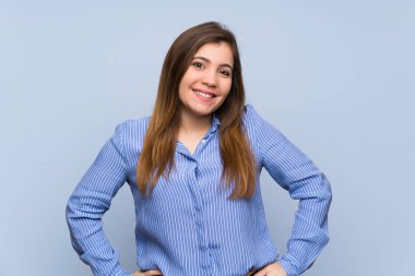 Izole mavi duvar üzerinde genç kız kalça kolları ile poz ve gülümseyerek