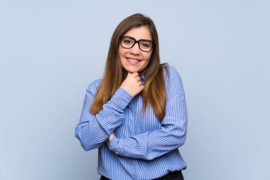 Gözlük ve gülümseyen izole mavi duvar üzerinde genç kız