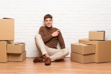 Yakışıklı genç adam yan parmak işaret kutuları arasında yeni bir evde hareket