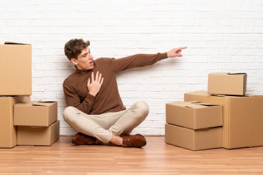 Yakışıklı genç adam yan parmak işaret kutuları arasında yeni bir evde hareket