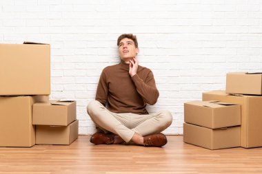 Yakışıklı genç adam kutuları arasında yeni bir evde bir fikir düşünme hareketli
