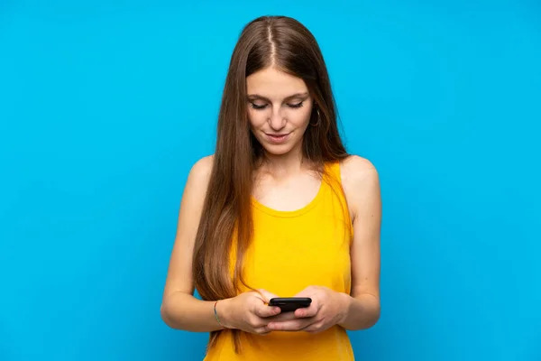 Młoda Kobieta Długimi Włosami Odizolowanej Niebieskiej Ścianie Wysyłając Wiadomość Telefonu — Zdjęcie stockowe