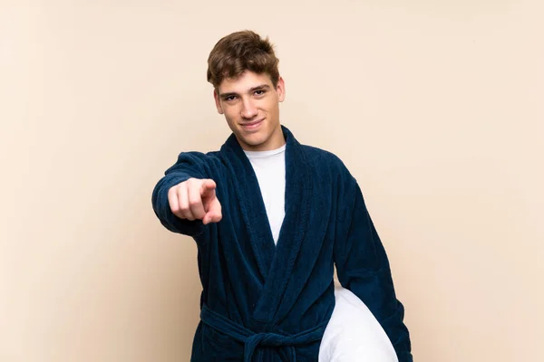Handsome young man in pajamas over isolated wall points finger at you with a confident expression