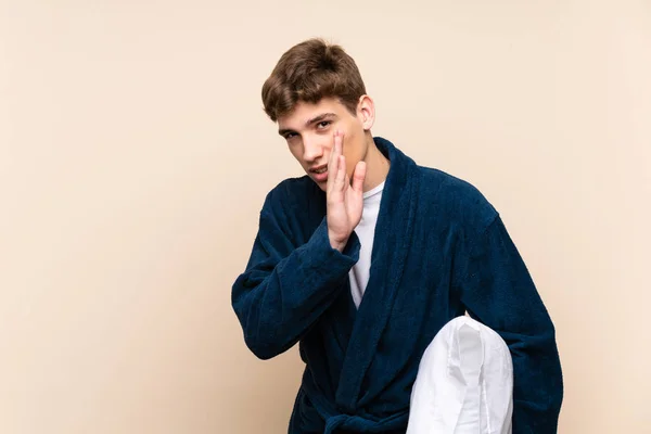 Handsome young man in pajamas over isolated wall whispering something