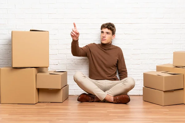 Handsome young man moving in new home among boxes touching on transparent screen