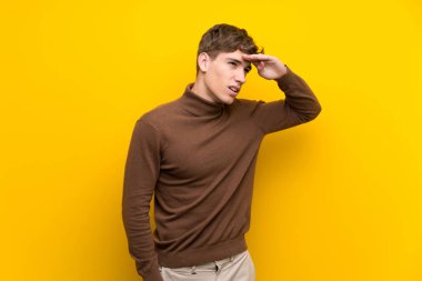 Izole sarı arka plan üzerinde Yakışıklı genç adam uzak el ile bir şey bakmak için bakıyor