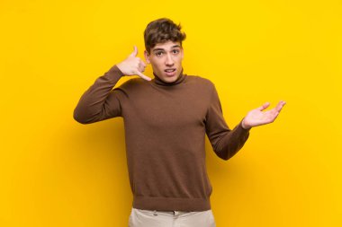Izole sarı arka plan üzerinde yakışıklı genç adam telefon jest yapma ve şüphe