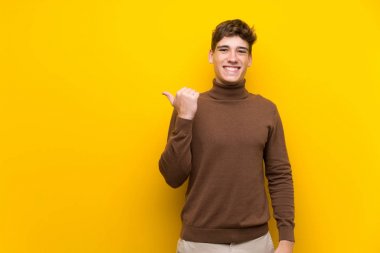 Izole sarı arka plan üzerinde yakışıklı genç adam bir ürün sunmak için yan işaret