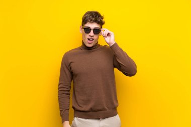 Gözlük lü izole sarı arka plan üzerinde Yakışıklı genç adam ve şaşırttı