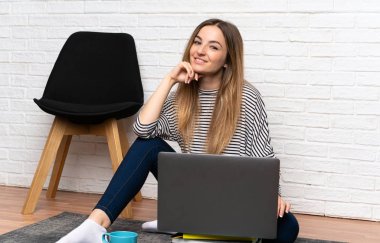 Genç bir kadın dizüstü bilgisayarıyla yerde oturuyor.