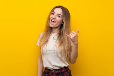 Izole sarı duvar üzerinde telefon jesti yapan genç kadın