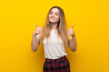 Izole sarı duvar üzerinde genç kadın jest kadar bir başparmak veren