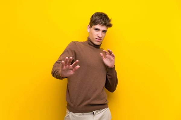 Handsome young man over isolated yellow background nervous stretching hands to the front