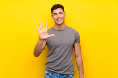 Izole sarı duvar üzerinde yakışıklı adam parmakları ile beş sayma