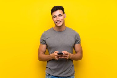Cep telefonu ile bir mesaj göndererek izole sarı duvar üzerinde Yakışıklı adam