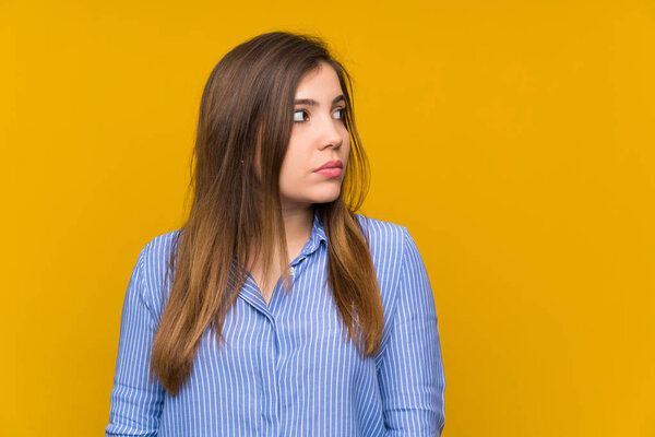 Молодая девушка в полосатой рубашке стоит и смотрит сбоку
