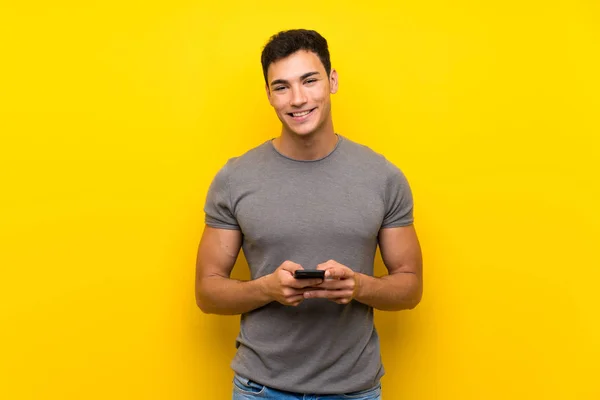 Hombre Guapo Sobre Aislada Pared Amarilla Enviando Mensaje Con Móvil —  Fotos de Stock