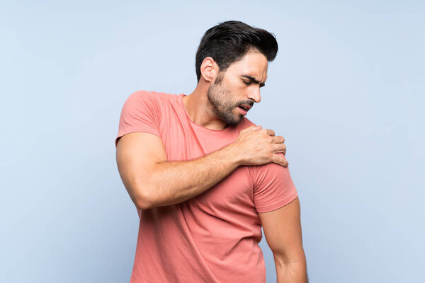 Красивый молодой человек в розовой рубашке на изолированном синем фоне страдает от боли в плече за то, что сделал усилие
