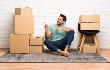 Yakışıklı genç adam yan parmak işaret kutuları arasında yeni bir evde hareket