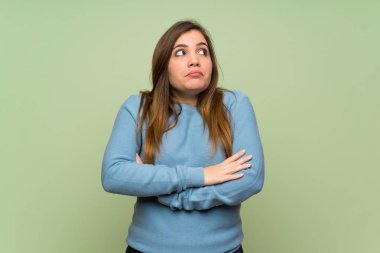 Omuzlarını kaldırırken yeşil duvar üzerinde şüphe jest genç kız