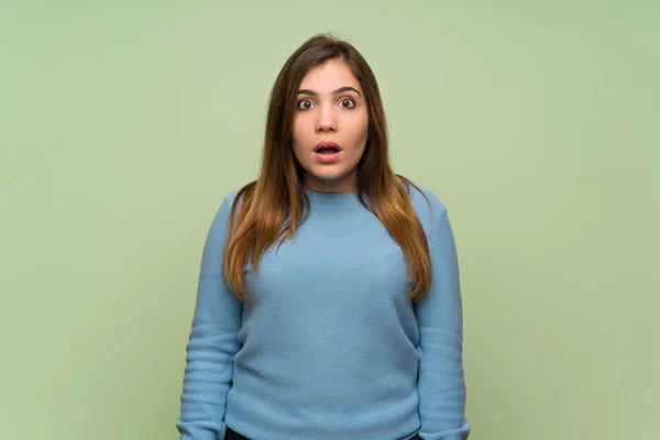 Young girl over green wall with surprise facial expression