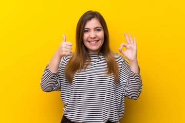Ok işareti ve başparmak yukarı jest gösteren sarı duvar üzerinde genç kız