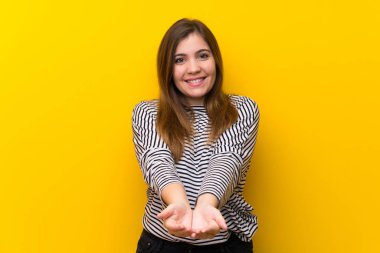 Bir reklam eklemek için avuç üzerinde copyspace hayali tutan sarı duvar üzerinde genç kız