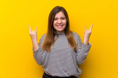 Sarı duvar üzerinde kaya jesti yapan genç kız