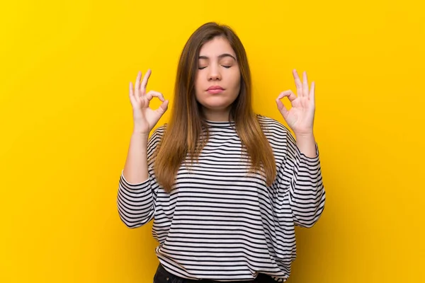 Young girl over yellow wall in zen pose
