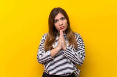 Sarı duvarın üstündeki genç kız avuç içini bir arada tutar. Kişi bir şey ister