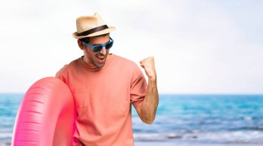 Yaz tatilinde şapkalı ve güneş gözlüklü adam zaferini kutluyor ve plajda ödül kazandığı için mutlu.