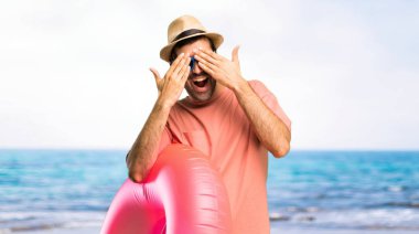 Yaz tatilinde şapkalı ve güneş gözlüklü bir adam gözlerini elleriyle kaplar. Sahilde neler olduğunu görmek için şaşırdım