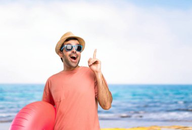 Yaz tatilinde şapkalı ve güneş gözlüklü adam sahilde parmağını kaldırırken çözümü gerçekleştirmeyi planlıyor.