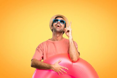 Yaz tatilinde şapkalı ve güneş gözlüklü adam işaret parmağıyla işaret ederek harika bir fikir ve turuncu arka plana bakıyor